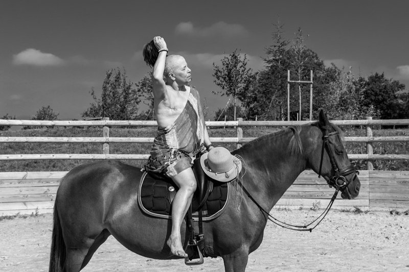 Portrait d'une participante à cheval tenant sa perruque levée, exposition Cicatrices